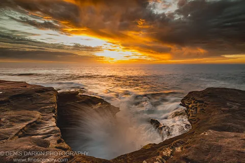A natural pool in the sandstone platform at Red Bluff collects blurred wave water as storm clouds part to reveal evening light.