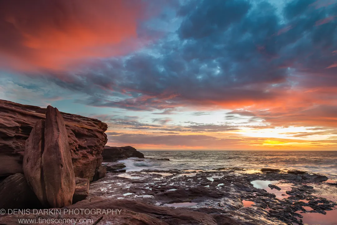 Weathered sandstone tide pools extend toward the horizon at Kalbarri as storm clouds split and warm light settles over the coastal shelf.