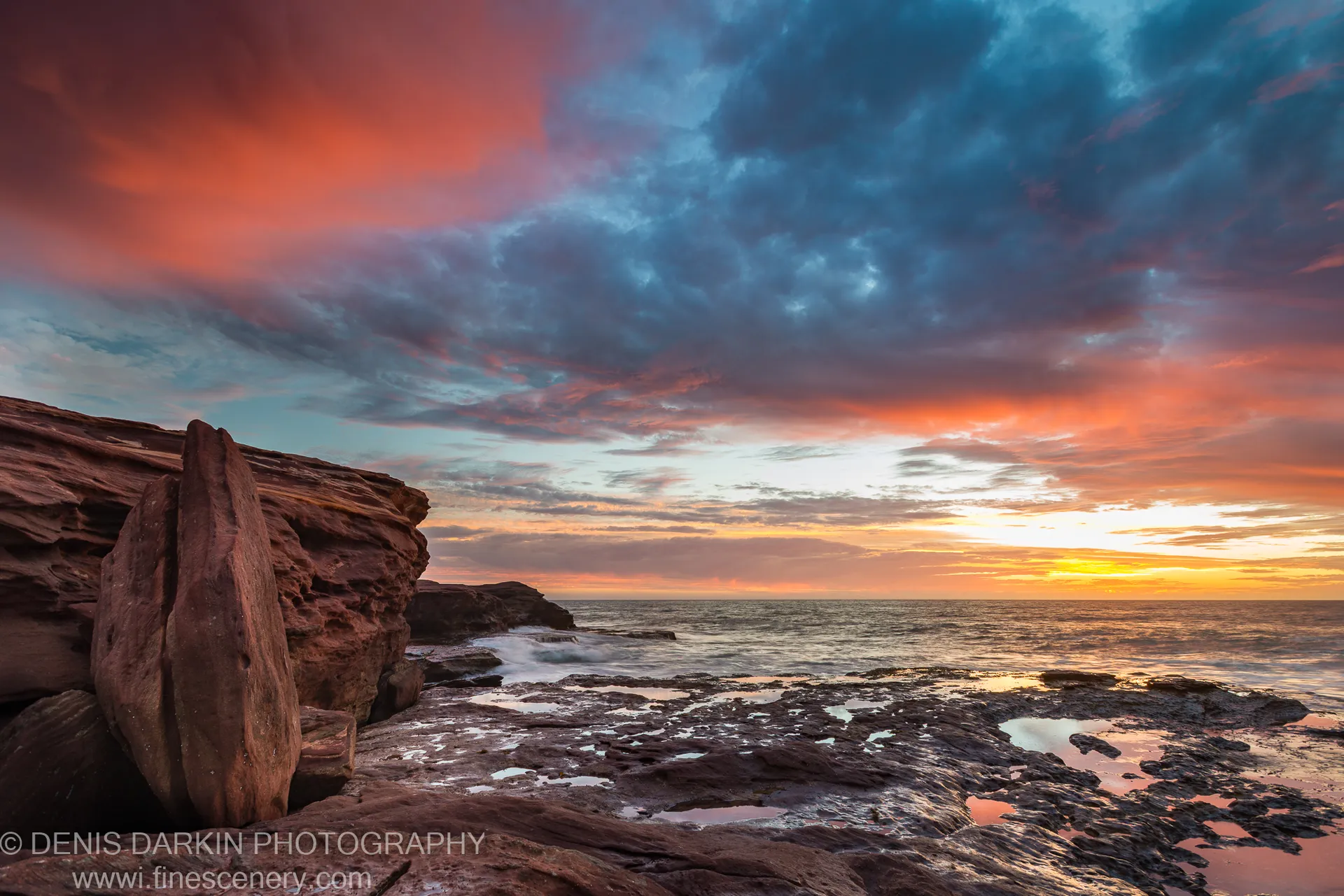 Weathered sandstone tide pools extend toward the horizon at Kalbarri as storm clouds split and warm light settles over the coastal shelf.