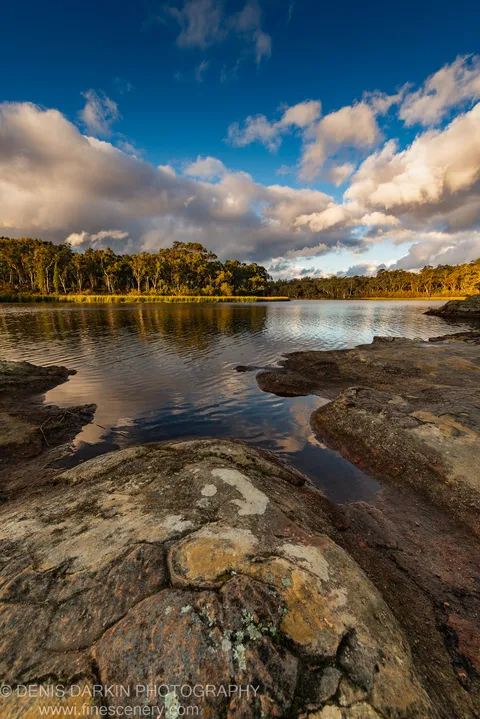 Weathered granite formations in the foreground face a still lake at Dunns Swamp, its surface reflecting billowing cumulus clouds in late afternoon.